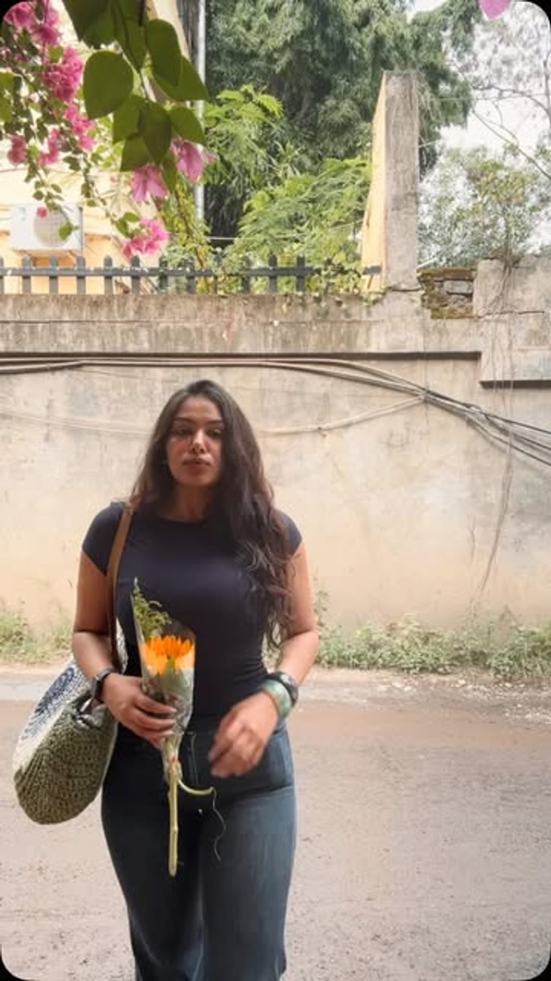 Standing against a plaster wall holding marigolds