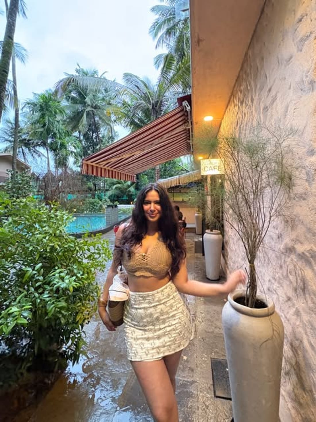Outside a cafe surrounded by palms, holding a drink